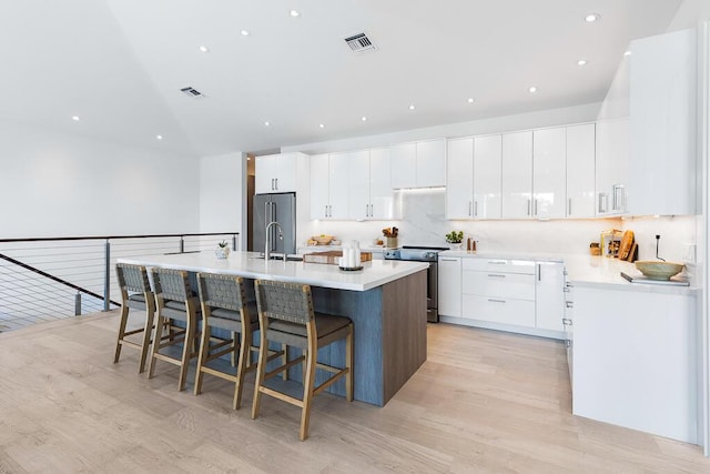 kitchen with a kitchen island with sink, white cabinetry, stainless steel appliances, a kitchen breakfast bar, and light hardwood / wood-style floors