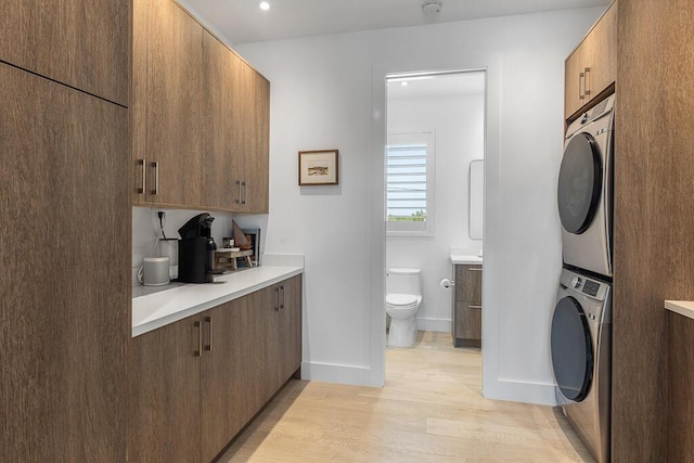 laundry area with cabinets, stacked washer and clothes dryer, and light hardwood / wood-style floors