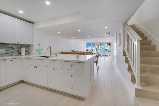 kitchen with white cabinetry, sink, backsplash, light hardwood / wood-style floors, and kitchen peninsula