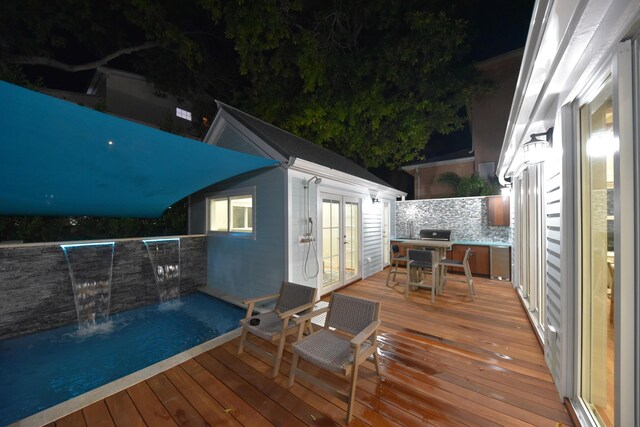 deck at twilight featuring french doors, outdoor dining space, an outdoor structure, and grilling area