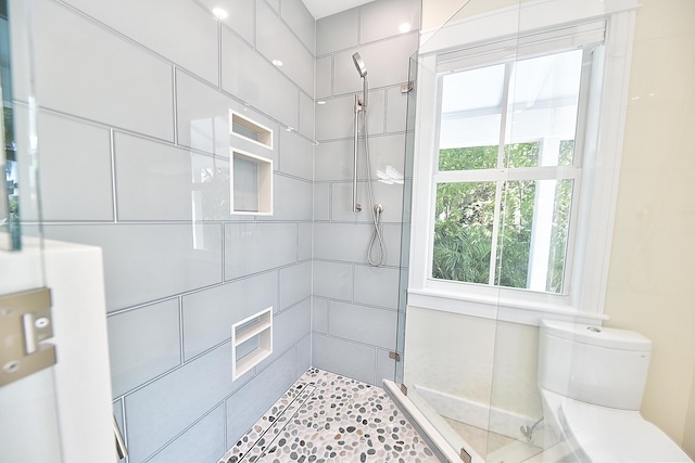 bathroom with toilet, a tile shower, and a healthy amount of sunlight