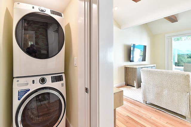 washroom featuring baseboards, stacked washer and clothes dryer, light wood-type flooring, and laundry area