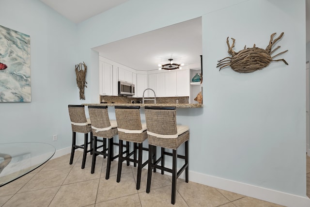 kitchen with light tile patterned flooring, a kitchen bar, kitchen peninsula, decorative backsplash, and white cabinets