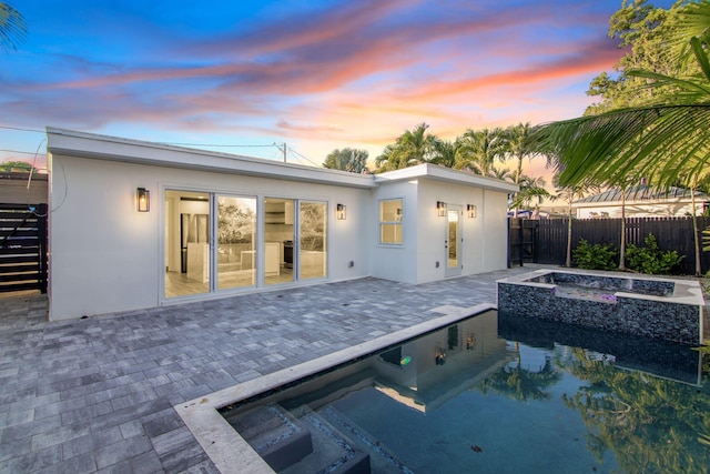 rear view of property featuring a fenced in pool, an in ground hot tub, fence, a patio area, and stucco siding