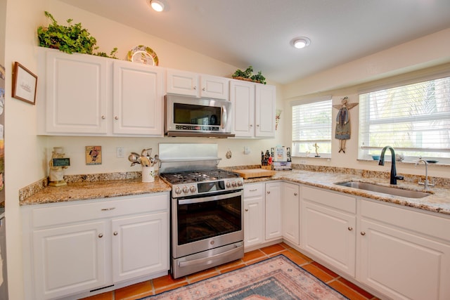 kitchen featuring appliances with stainless steel finishes, lofted ceiling, white cabinets, and a sink