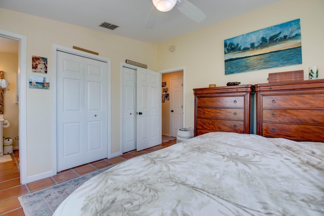 bedroom with ceiling fan, tile patterned flooring, visible vents, baseboards, and two closets