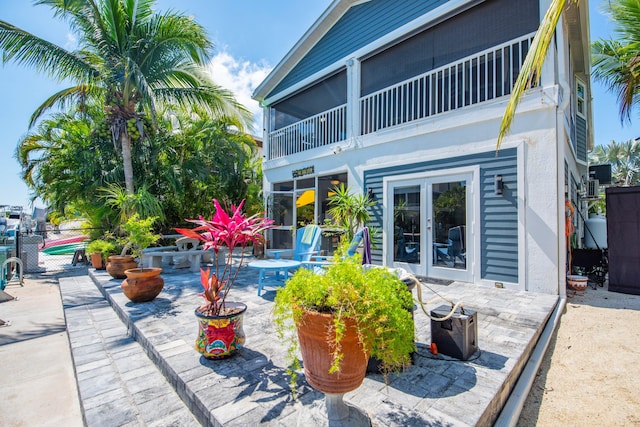 rear view of property with a patio, a balcony, fence, french doors, and stucco siding