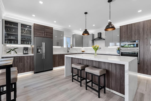 kitchen featuring pendant lighting, sink, stainless steel appliances, a kitchen island, and wall chimney exhaust hood