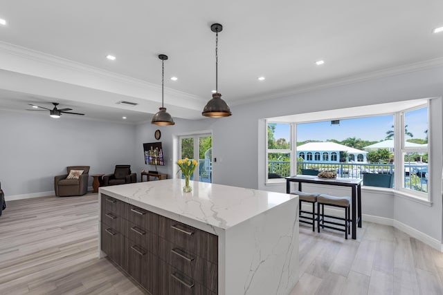 kitchen with a kitchen island, pendant lighting, ornamental molding, light stone countertops, and light hardwood / wood-style flooring