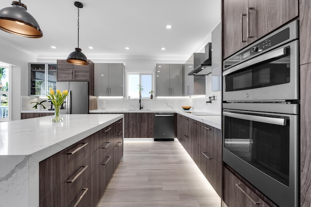 kitchen with hanging light fixtures, ornamental molding, light stone counters, black appliances, and wall chimney range hood