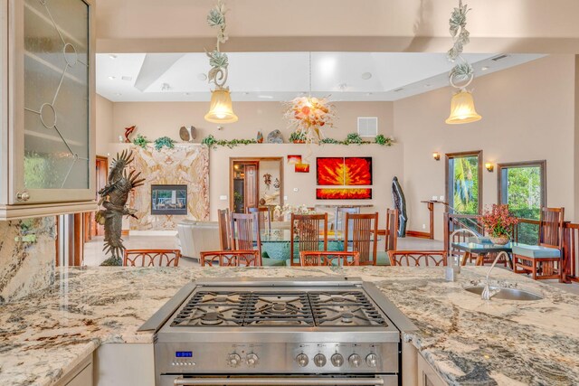 kitchen with light stone counters, stainless steel range with gas cooktop, decorative light fixtures, and a tray ceiling