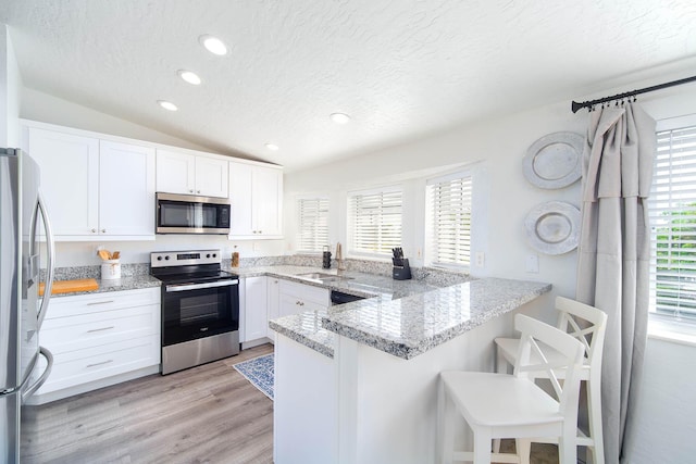 22988 Port Royal Ln, Cudjoe, FL 33042 - kitchen featuring appliances with stainless steel finishes, a textured ceiling, a peninsula, white cabinets, and light wood-type flooring