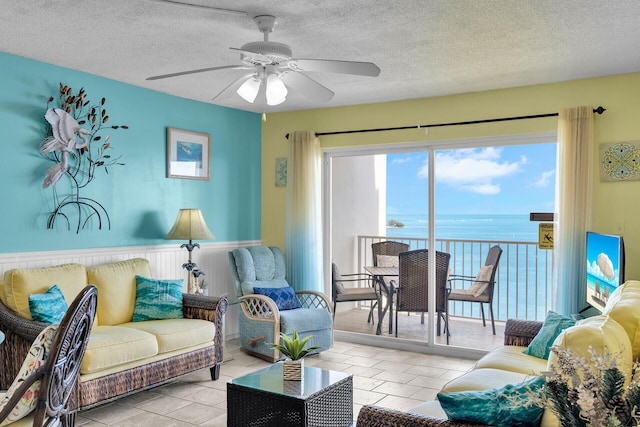 living room featuring a water view, ceiling fan, and a textured ceiling