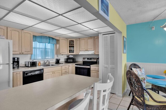 kitchen with sink, a paneled ceiling, light tile patterned floors, light brown cabinets, and black appliances