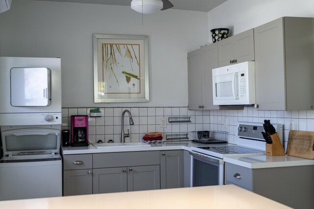 kitchen with sink, white appliances, gray cabinetry, backsplash, and stacked washer and clothes dryer