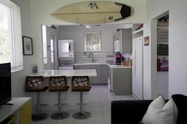 kitchen featuring sink, white appliances, gray cabinets, stacked washer and clothes dryer, and kitchen peninsula