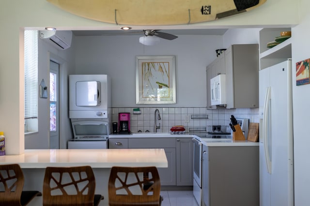 kitchen featuring stacked washer and clothes dryer, sink, a breakfast bar area, gray cabinets, and white appliances