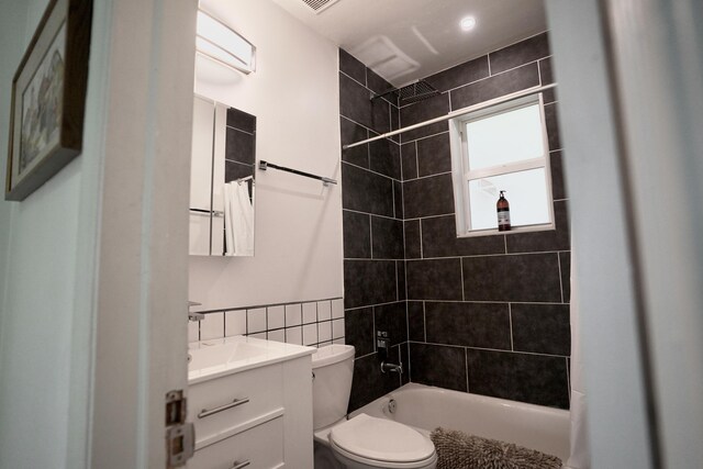 full bathroom featuring vanity, toilet, tiled shower / bath combo, and tile walls