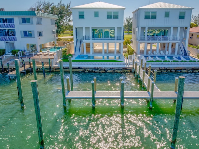 back of house with a water view, a balcony, and a pool