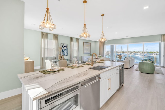 kitchen with sink, white cabinets, stainless steel dishwasher, light stone countertops, and a center island with sink