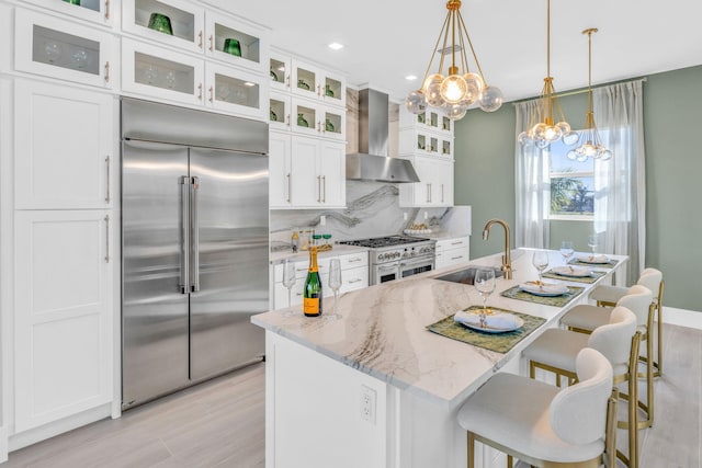 kitchen featuring decorative light fixtures, high quality appliances, an island with sink, sink, and wall chimney exhaust hood