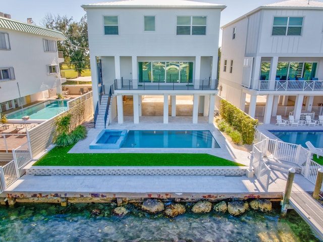 rear view of house featuring a swimming pool with hot tub, a patio area, a balcony, and a water view