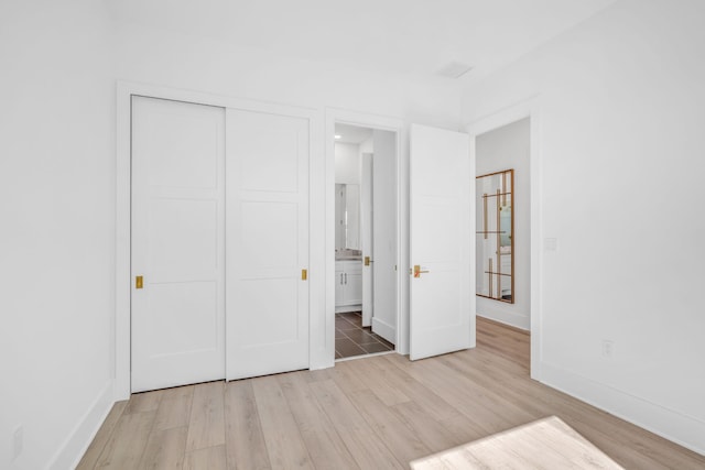 unfurnished bedroom with ensuite bath, light wood-type flooring, and a closet