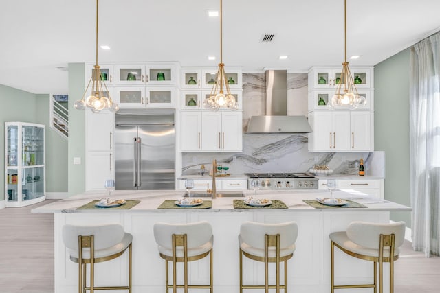 kitchen with stainless steel built in refrigerator, an island with sink, a kitchen breakfast bar, and wall chimney exhaust hood