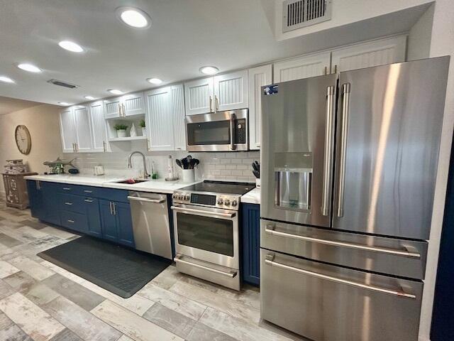 kitchen featuring sink, blue cabinetry, white cabinetry, backsplash, and stainless steel appliances