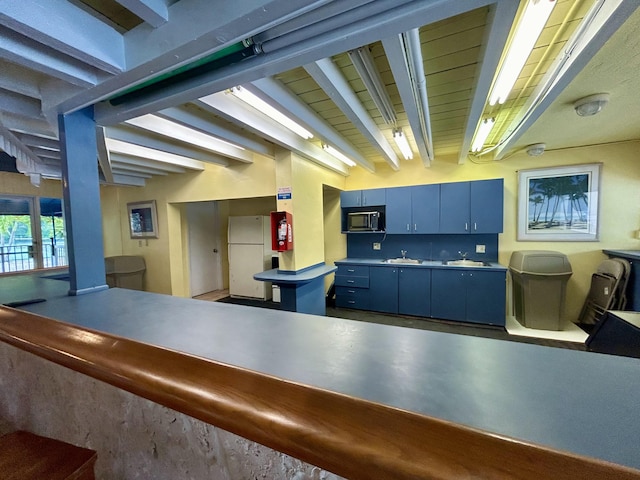 kitchen with blue cabinets, sink, concrete floors, white fridge, and beam ceiling