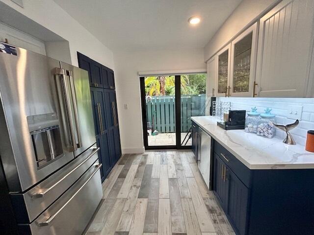 kitchen with appliances with stainless steel finishes, blue cabinets, white cabinetry, light stone countertops, and light wood-type flooring