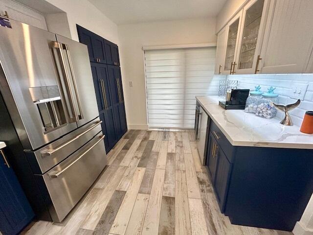 kitchen with blue cabinets, white cabinets, light stone counters, high end fridge, and light wood-type flooring