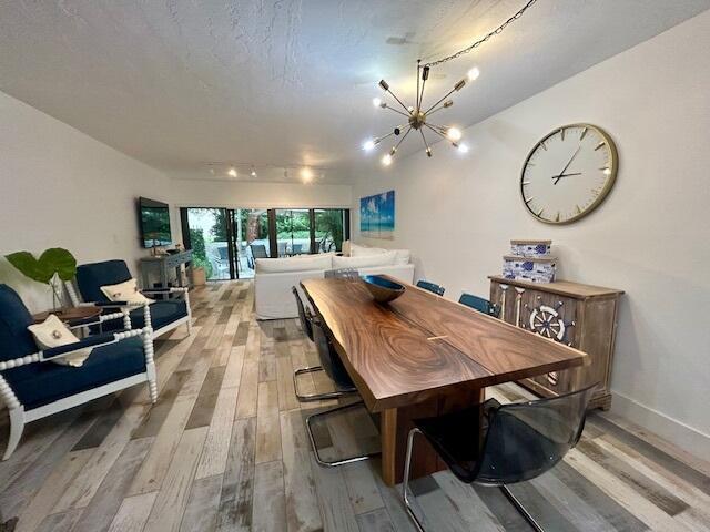 dining room featuring rail lighting, a textured ceiling, a chandelier, and light hardwood / wood-style flooring