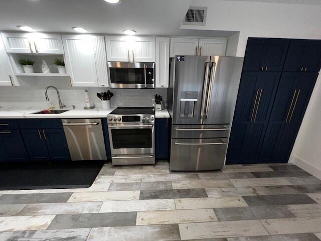 kitchen with sink, appliances with stainless steel finishes, white cabinetry, tasteful backsplash, and blue cabinets