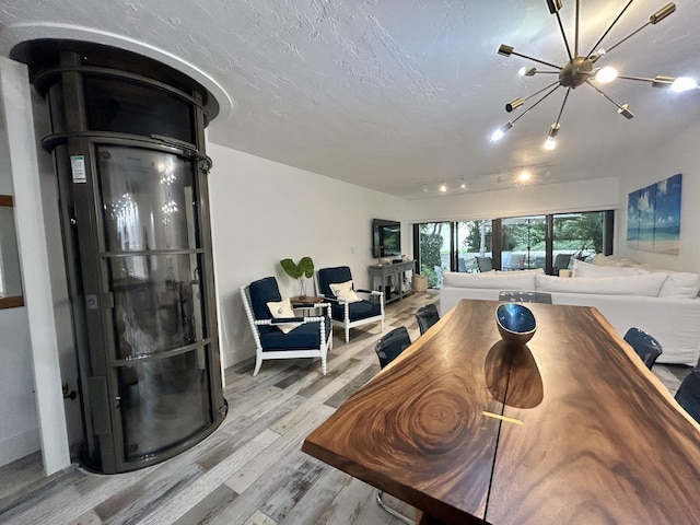 dining room featuring rail lighting, a notable chandelier, a textured ceiling, and light hardwood / wood-style flooring