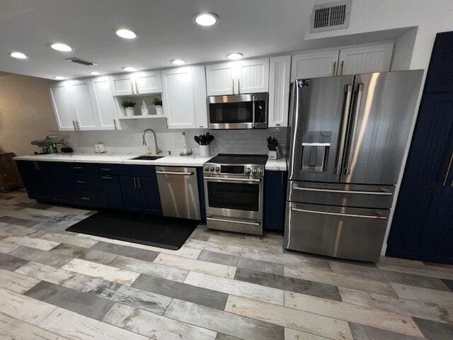 kitchen with tasteful backsplash, blue cabinets, sink, white cabinets, and stainless steel appliances