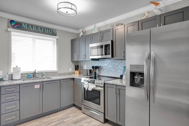 kitchen featuring sink, backsplash, stainless steel appliances, light stone counters, and ornamental molding