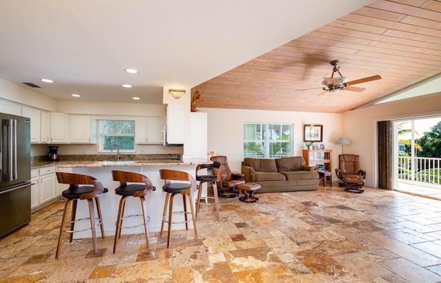 kitchen featuring a healthy amount of sunlight, high end fridge, white cabinets, and a breakfast bar