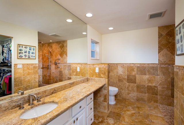 bathroom with tile walls, vanity, toilet, and tiled shower