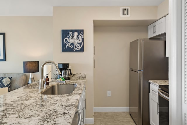 kitchen with sink, light tile patterned floors, electric range oven, light stone counters, and white cabinets