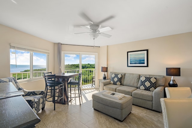 tiled living room featuring a healthy amount of sunlight, ceiling fan, and a water view