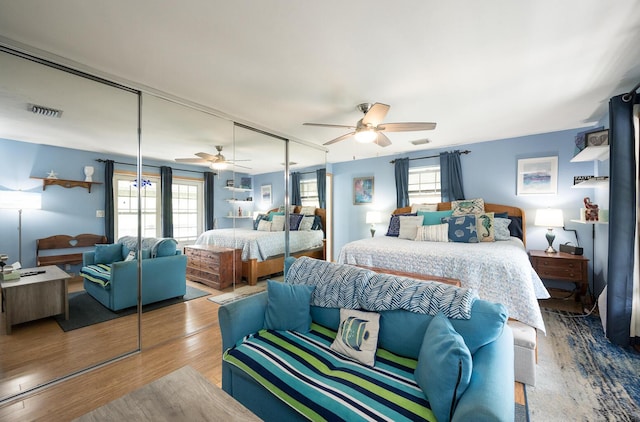 bedroom with multiple windows, hardwood / wood-style flooring, ceiling fan, and a closet