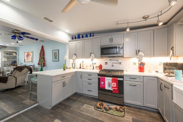 kitchen featuring dark wood-type flooring, ceiling fan, appliances with stainless steel finishes, decorative backsplash, and kitchen peninsula