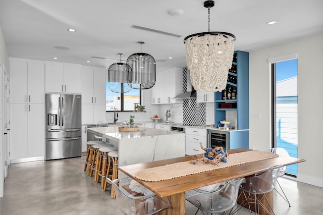 kitchen featuring stainless steel fridge, white cabinetry, a kitchen island, decorative light fixtures, and wall chimney exhaust hood