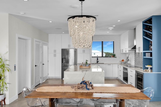 kitchen with pendant lighting, wall chimney range hood, stainless steel appliances, white cabinets, and decorative backsplash