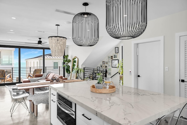 kitchen featuring white cabinetry, stainless steel oven, decorative light fixtures, light stone countertops, and ceiling fan with notable chandelier