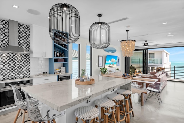 kitchen featuring white cabinetry, wall chimney exhaust hood, oven, and hanging light fixtures