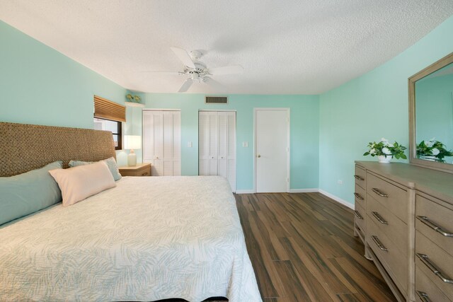 bedroom with multiple closets, ceiling fan, a textured ceiling, and dark hardwood / wood-style flooring