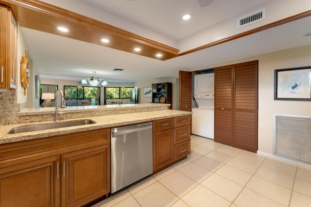 kitchen featuring stacked washer and dryer, sink, light stone counters, stainless steel dishwasher, and pendant lighting