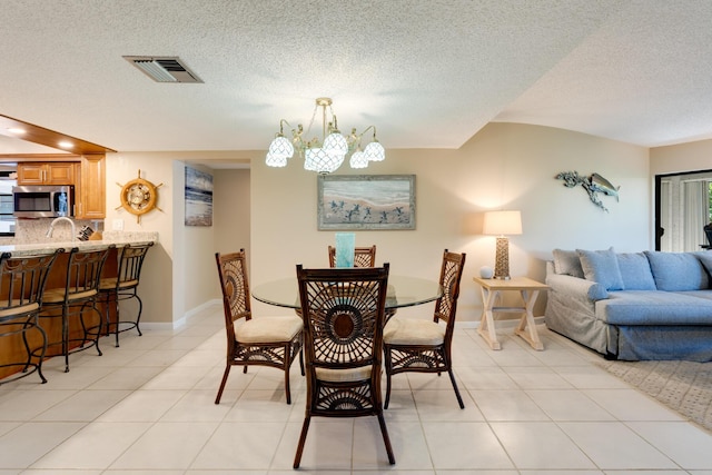 dining area featuring light tile patterned floors, a notable chandelier, sink, and a textured ceiling